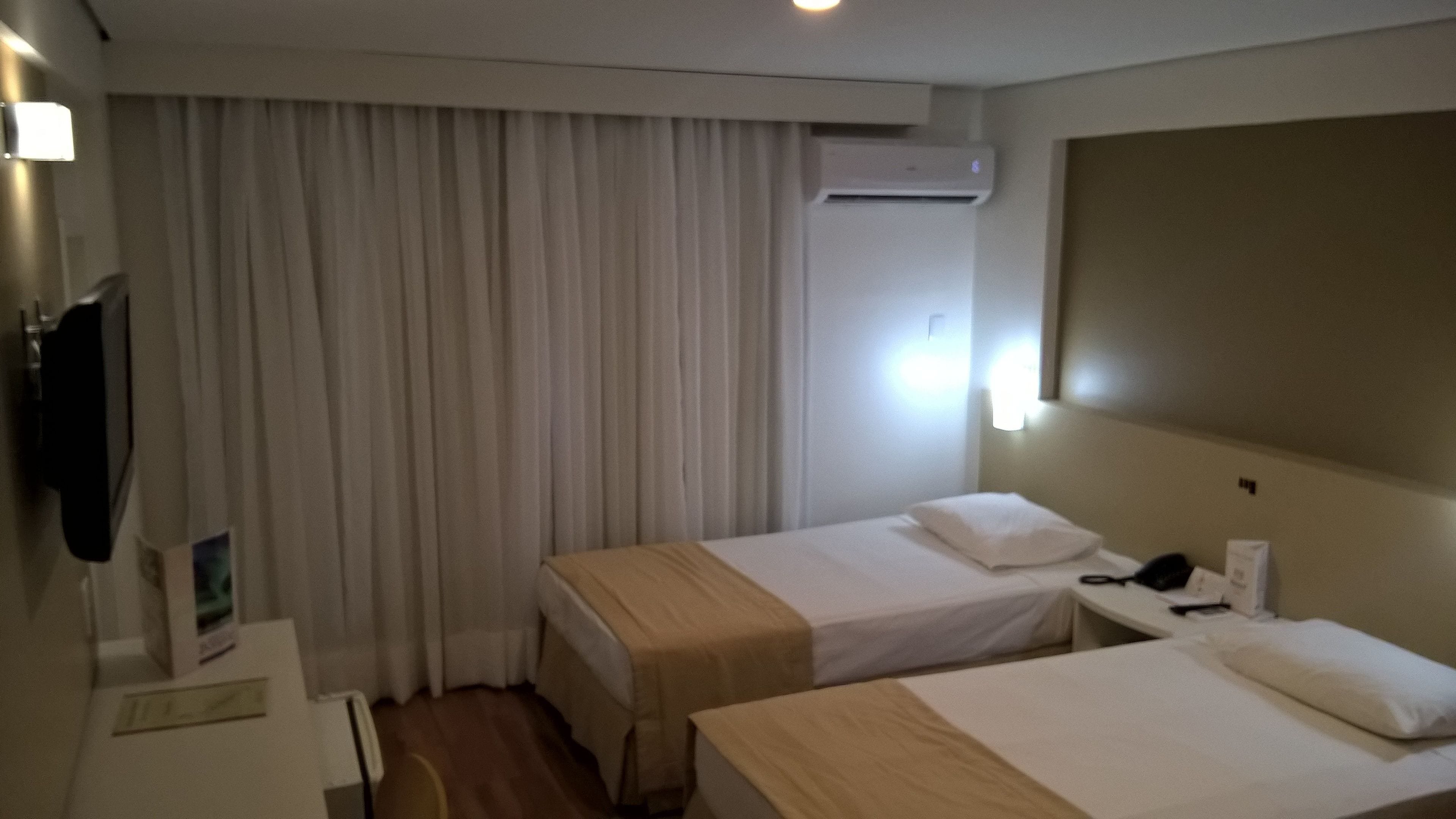 Ein Hotelzimmer mit zwei Betten, einem Schreibtisch, einem Stuhl, einem Fernseher und einer Klimaanlage.
