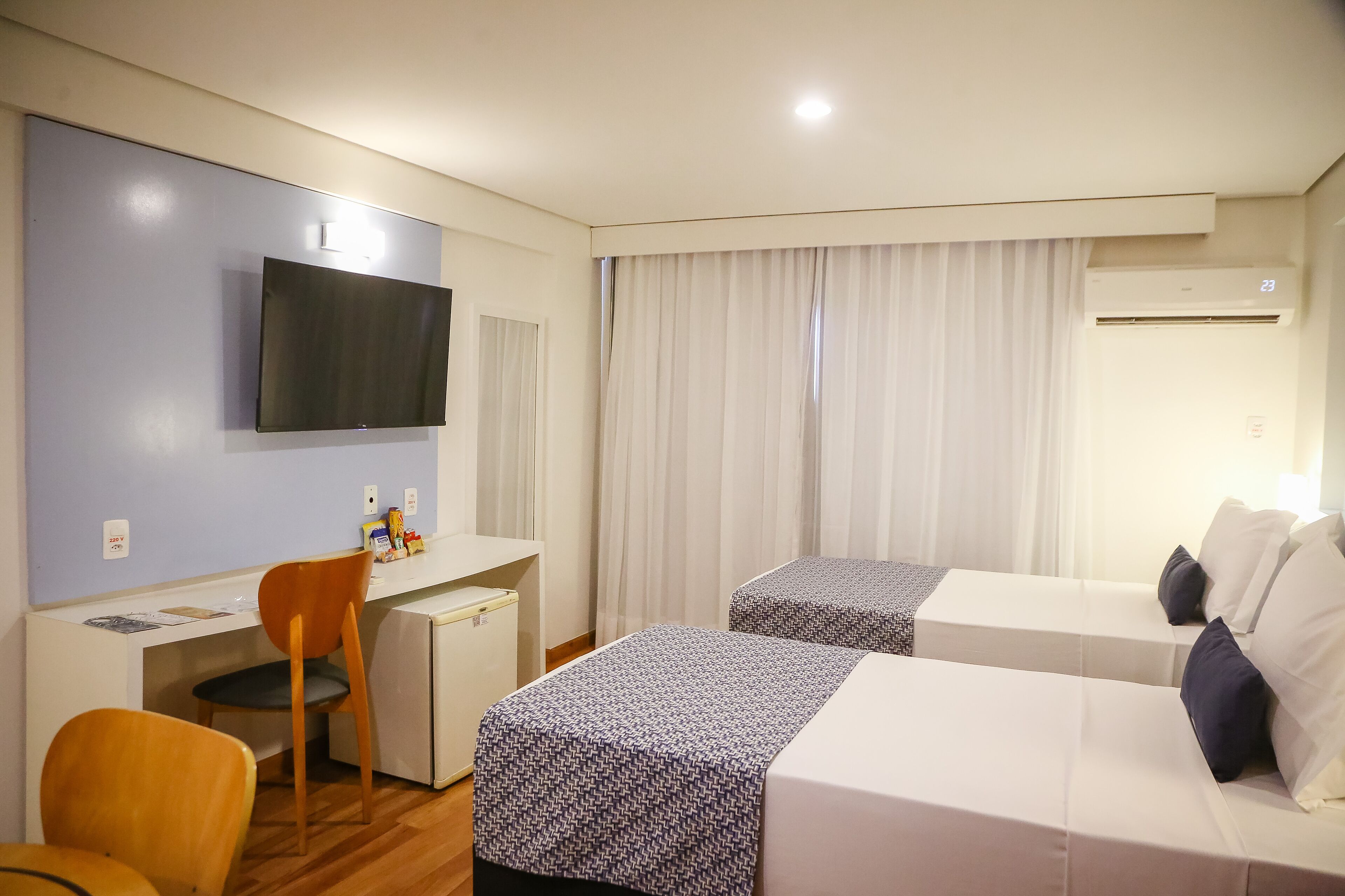 Habitación de hotel con escritorio, dos camas, televisor y aire acondicionado.