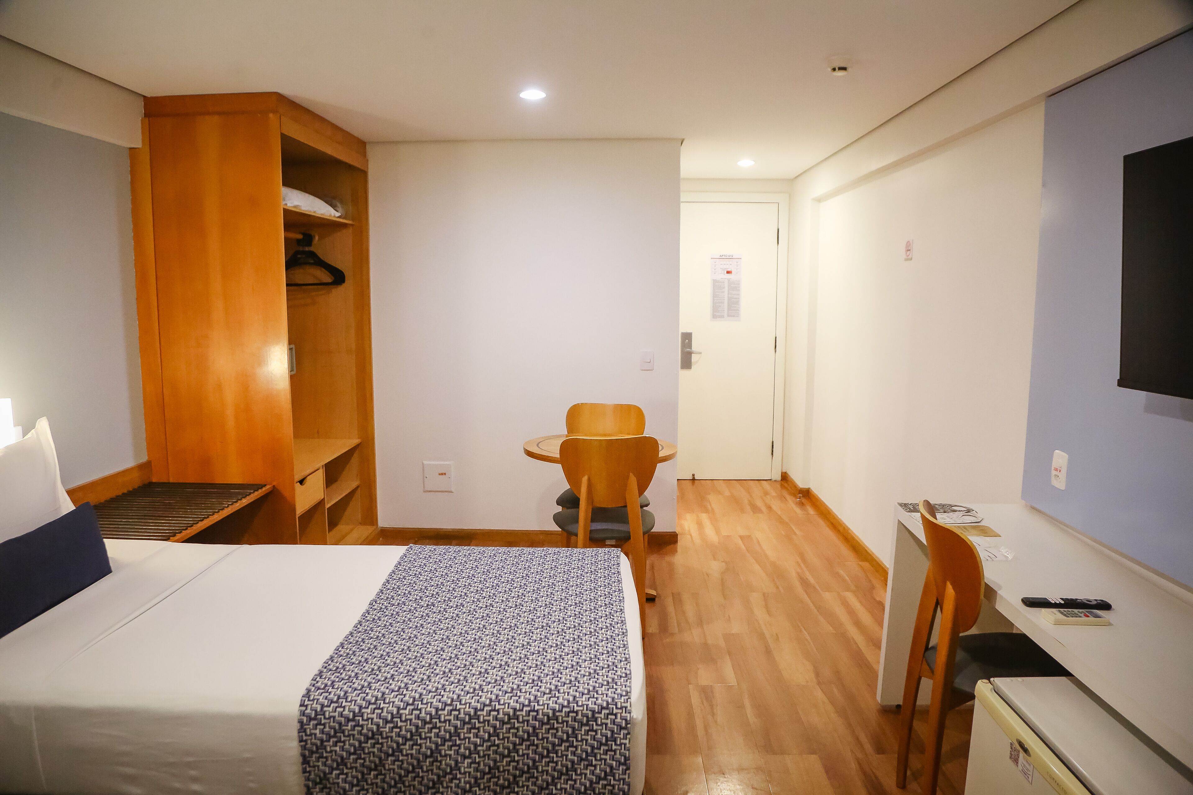 A hotel room with a bed, a wooden wardrobe, a desk with a chair, and a television.