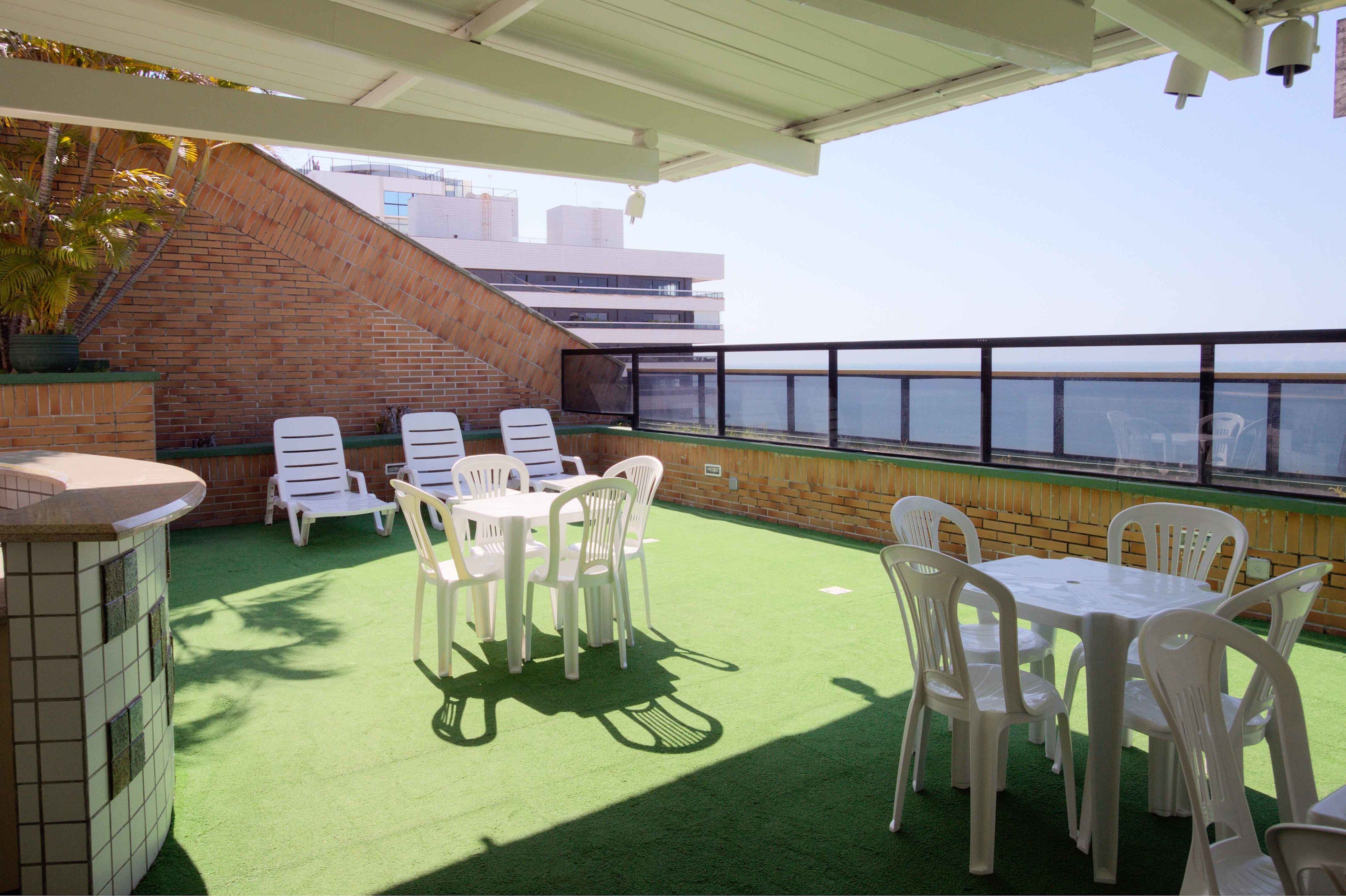 An outdoor patio with green artificial turf, white plastic chairs, and a table.