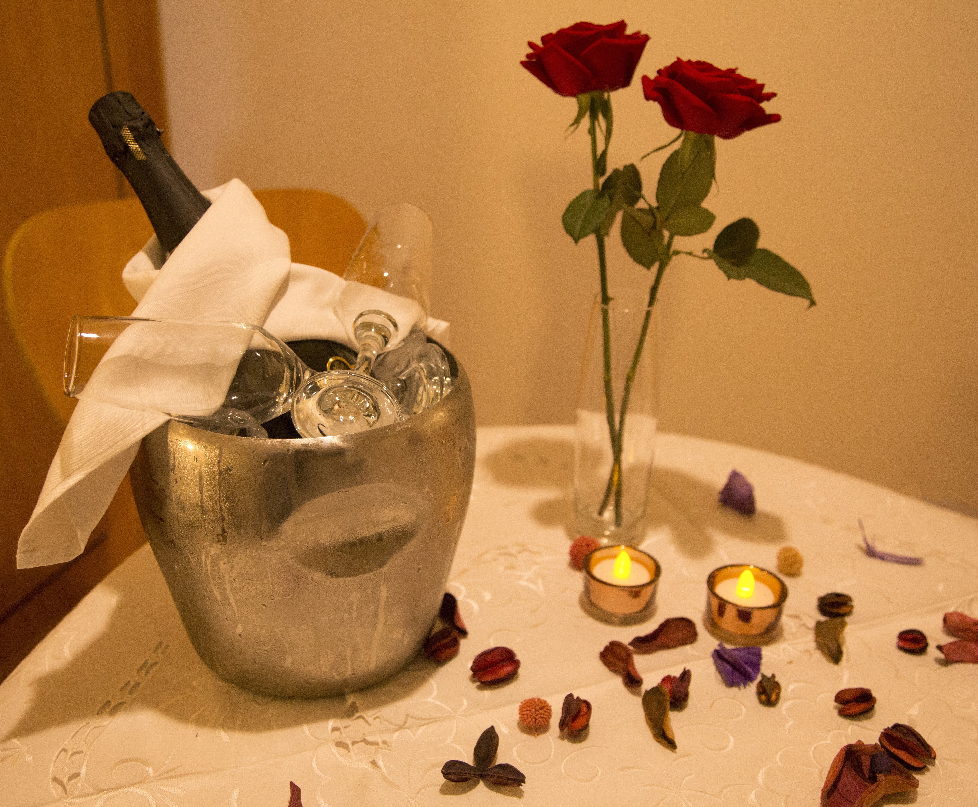 A table with a metal bucket containing a bottle and glasses, a vase with roses, and two lit candles.