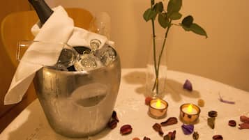 Ein Tisch mit einem Metallkübel, der eine Flasche und Gläser enthält, eine Vase mit Rosen und zwei brennende Kerzen.