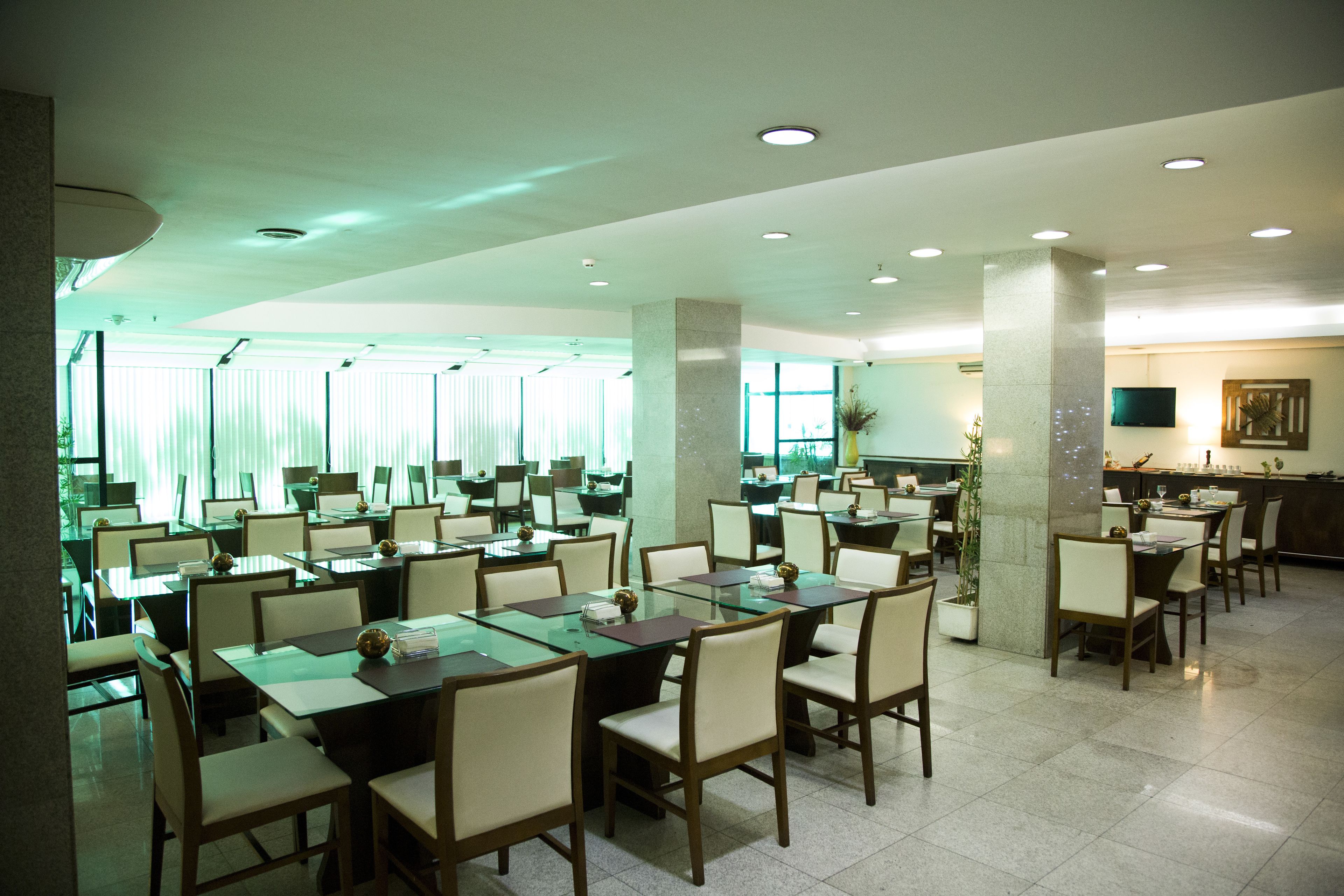 Un'ampia sala da pranzo con numerosi tavoli e sedie, grandi finestre con tende e un arredamento moderno.