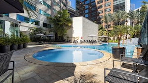 A swimming pool with lounge chairs and umbrellas, surrounded by palm trees and modern buildings. - Radisson Hotel Vila Olimpia (São Paulo)