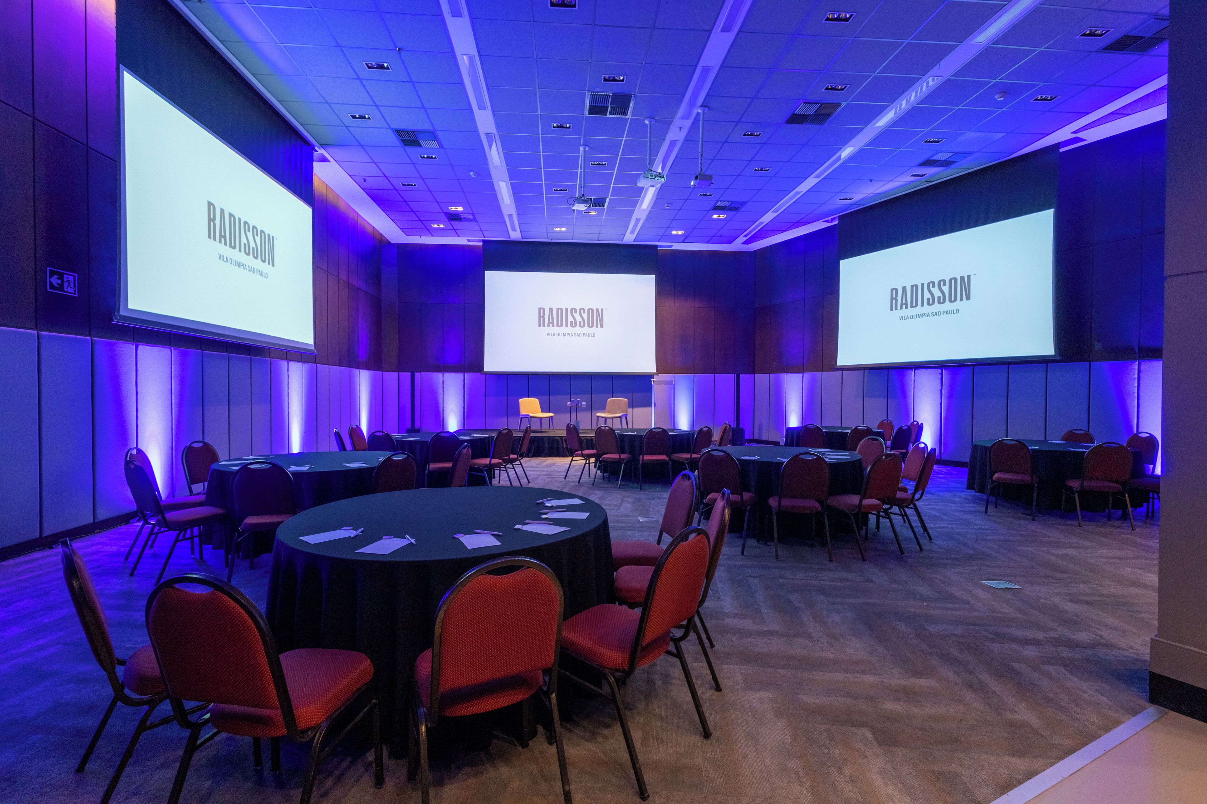 A conference room with round tables, red chairs, and large screens displaying the Radisson logo.