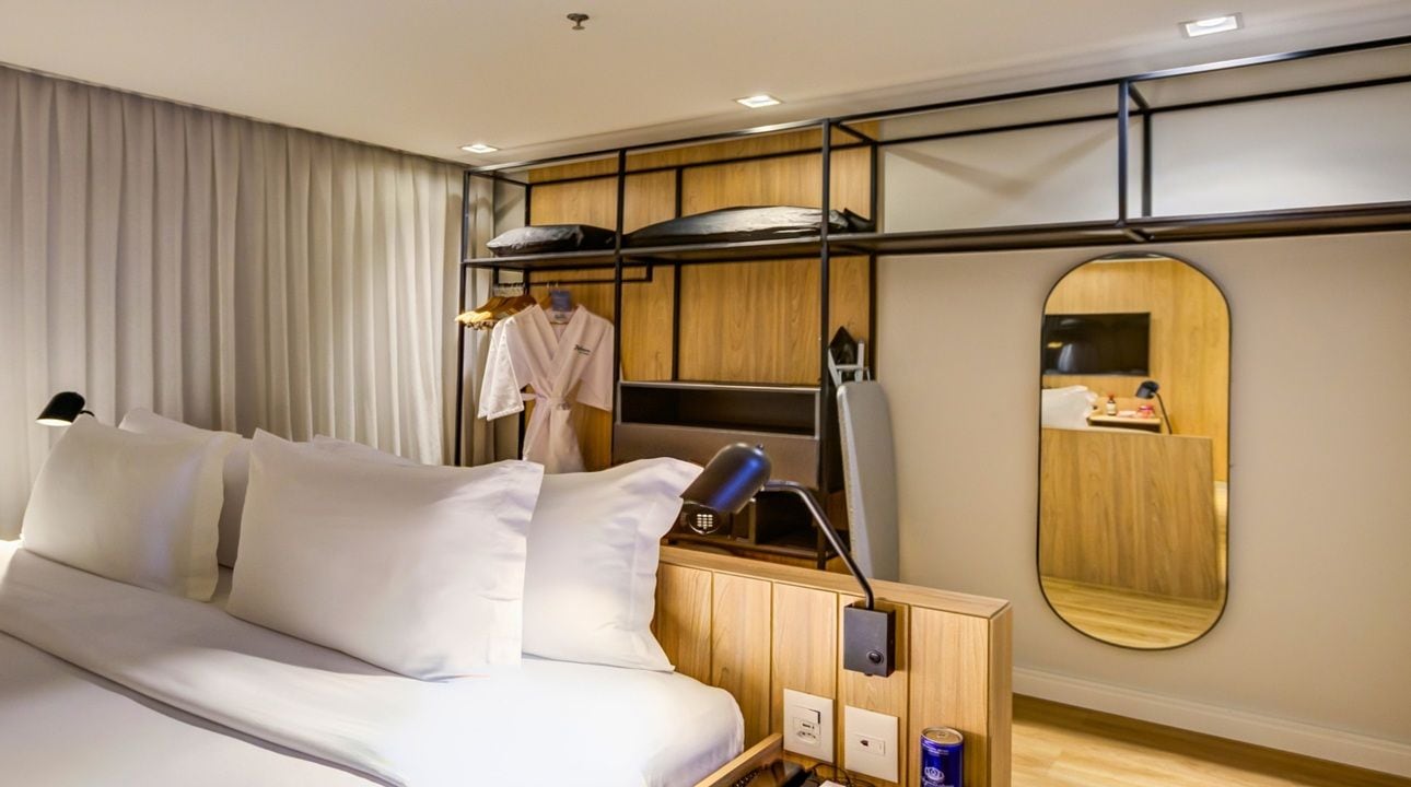 A hotel room with a bunk bed, a bedside table with a lamp, a mirror, and a wardrobe.