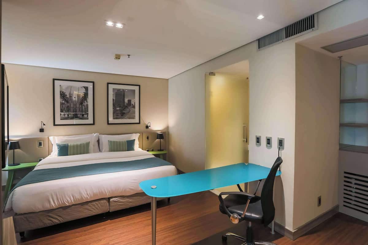 Une chambre d’hôtel avec un lit, un bureau et deux tableaux encadrés au mur.