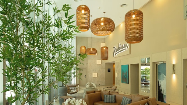 A modern lobby with a large sectional sofa, a potted plant, and hanging wicker lamps. - Radisson Hotel Vila Olimpia (São Paulo)
