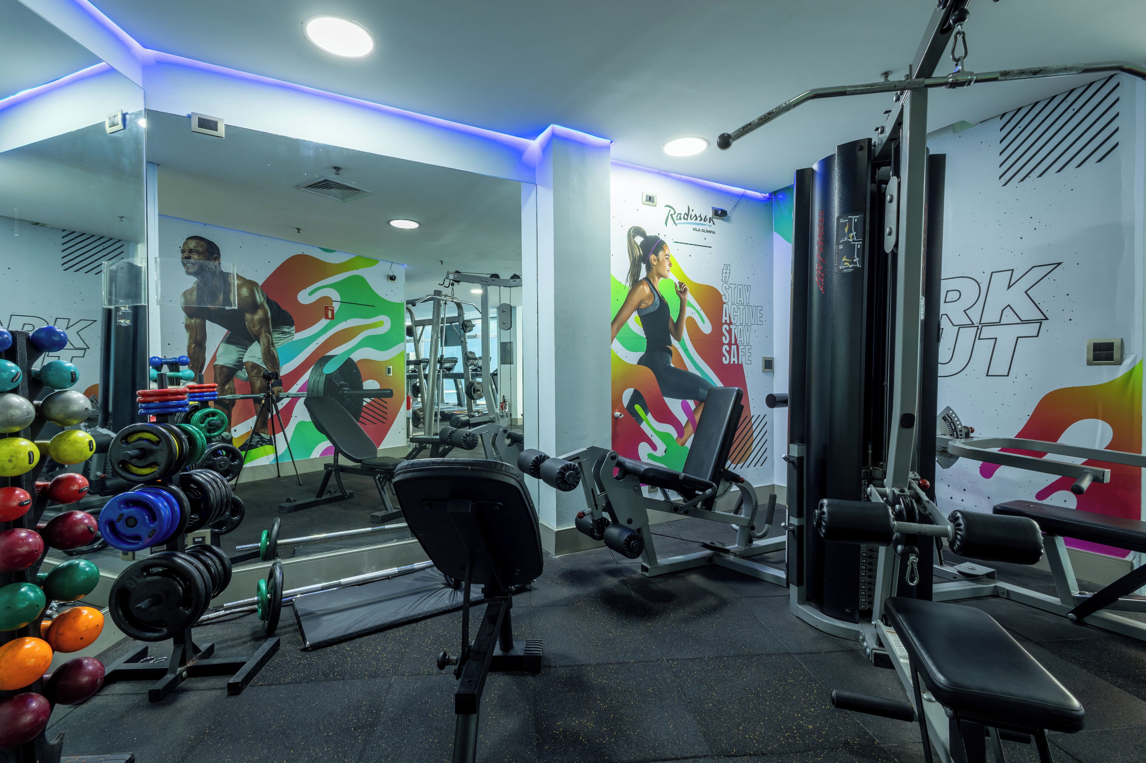 Un gimnasio con equipamiento de levantamiento de pesas, espejos y decoración mural motivacional.