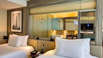 Une chambre d’hôtel avec deux lits, un grand miroir, une télévision et un tableau représentant une vue sur la ville accroché au mur.