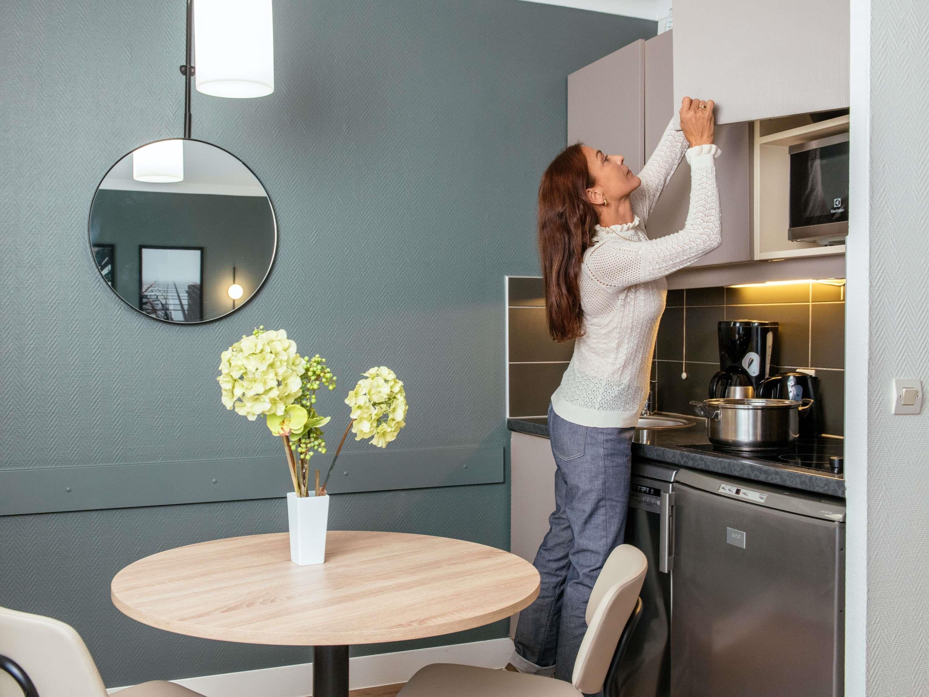 Una mujer en una cocina con un microondas, una estufa y una mesa redonda con un florero.