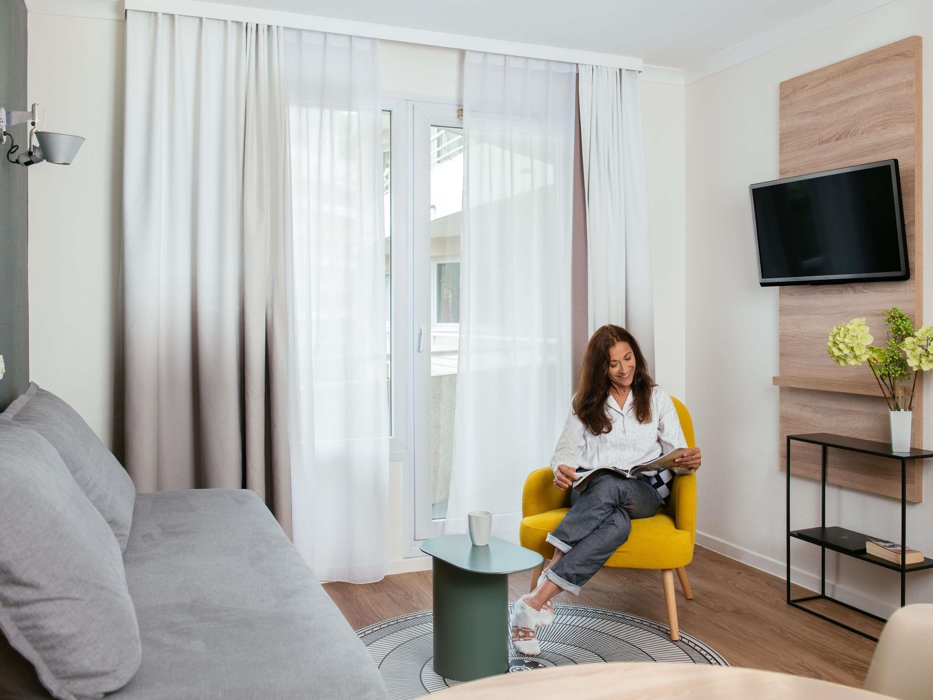 Un salon moderne avec un canapé, un fauteuil jaune, une petite table et un téléviseur fixé au mur.