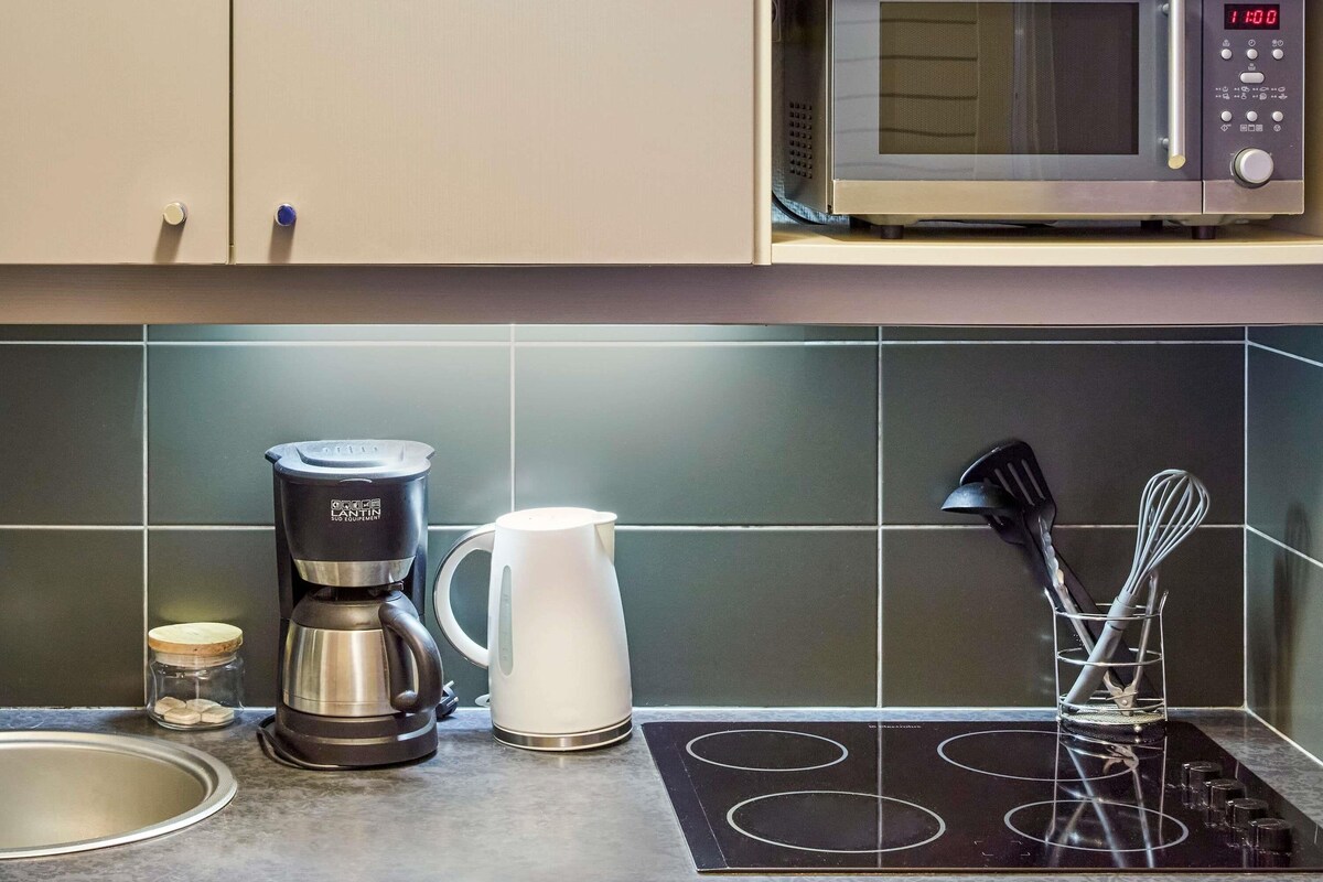 A kitchen with a microwave, coffee maker, kettle, and a stovetop.