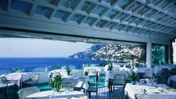 A restaurant with outdoor seating overlooking the sea, featuring a tiled floor and a ceiling with a geometric pattern.