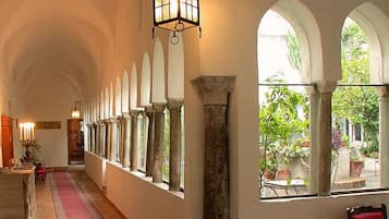 A corridor with arched windows, a red carpet, and a hanging light fixture.