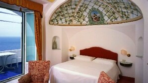 Un dormitorio con cama, dos sillones, vista al mar y un techo decorativo.
