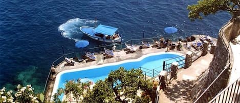 Ein Poolbereich mit einem Boot in der Nähe, umgeben von Liegestühlen und Sonnenschirmen.