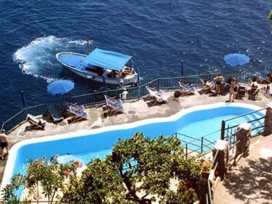 Zona de piscina con un barco amarrado cerca, rodeada de sillas de descanso y sombrillas.