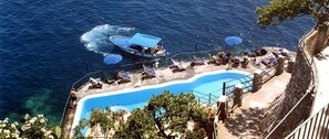 A pool area with a boat docked nearby, surrounded by lounge chairs and umbrellas. - Luna Convento (Amalfi)