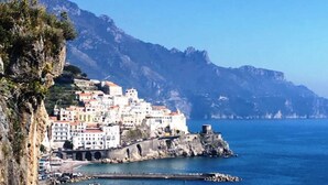 Un pueblo costero con edificios sobre un acantilado con vistas al mar, una estructura fortificada y un cielo azul despejado.