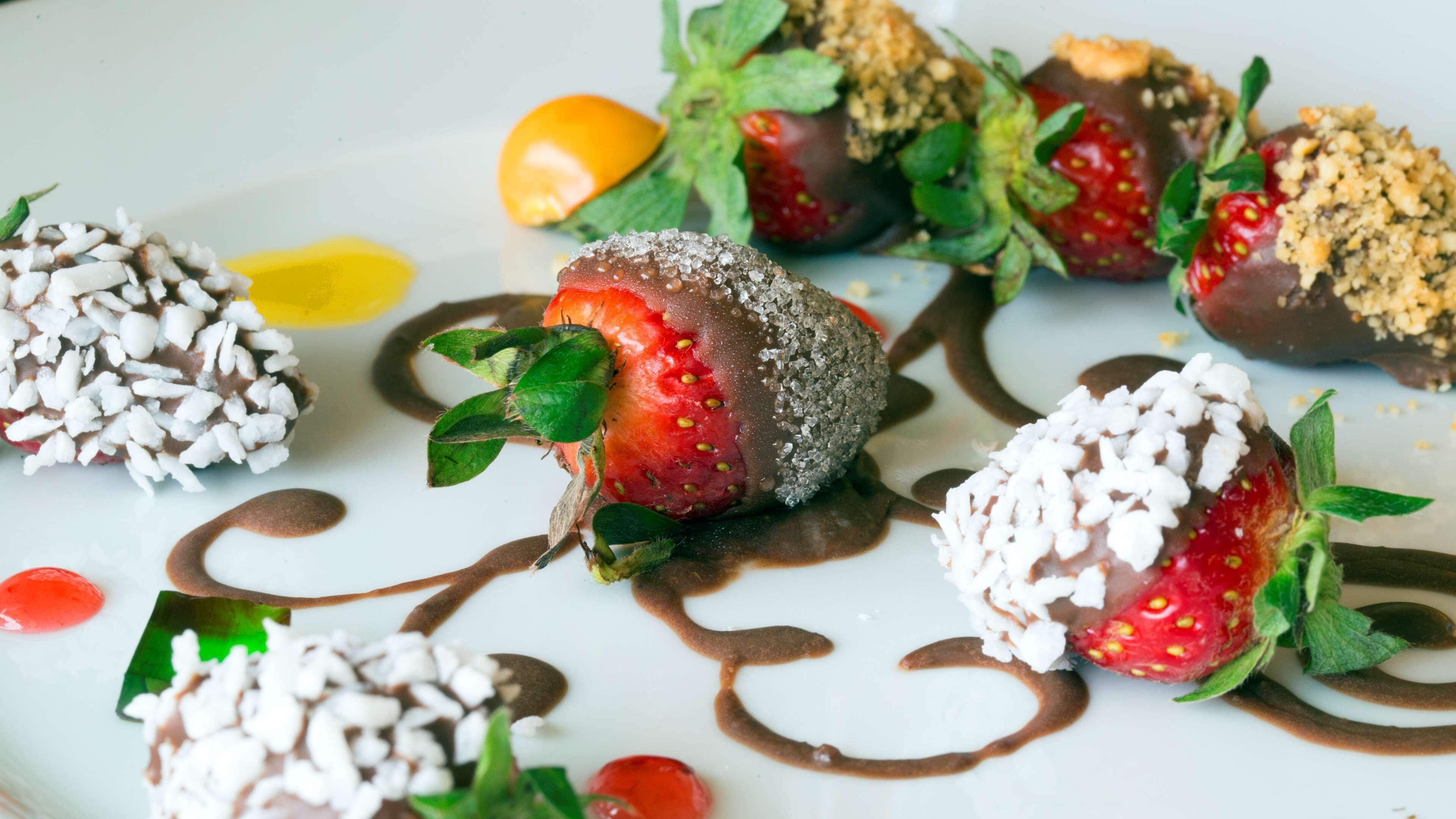 Un plato de postre con fresas bañadas en chocolate, virutas de chocolate blanco y un hilo de salsa de chocolate.