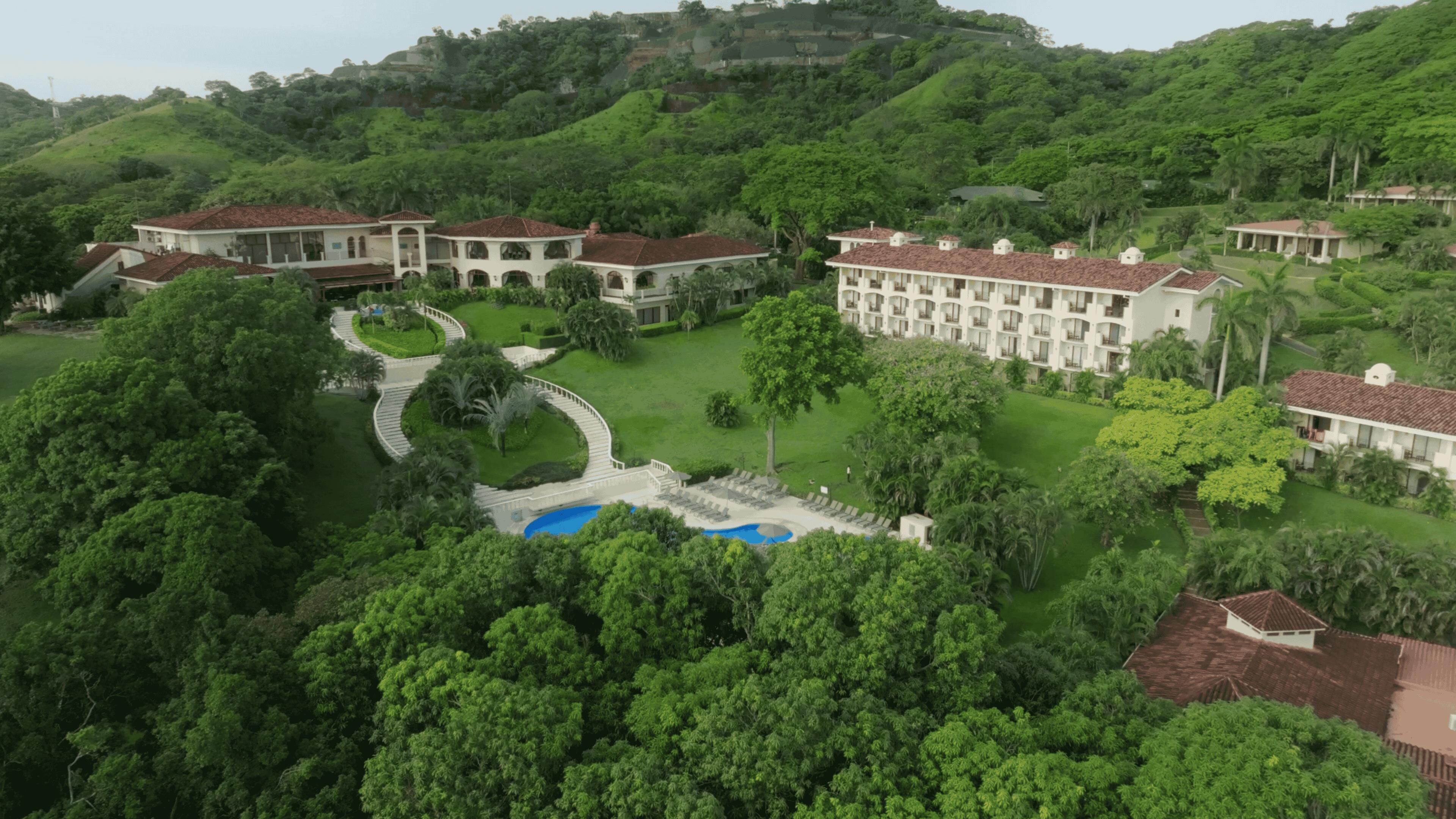A large resort with multiple buildings, a swimming pool, and lush greenery.