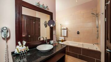 A bathroom with a sink, mirror, towel rack, shower, and a telephone.