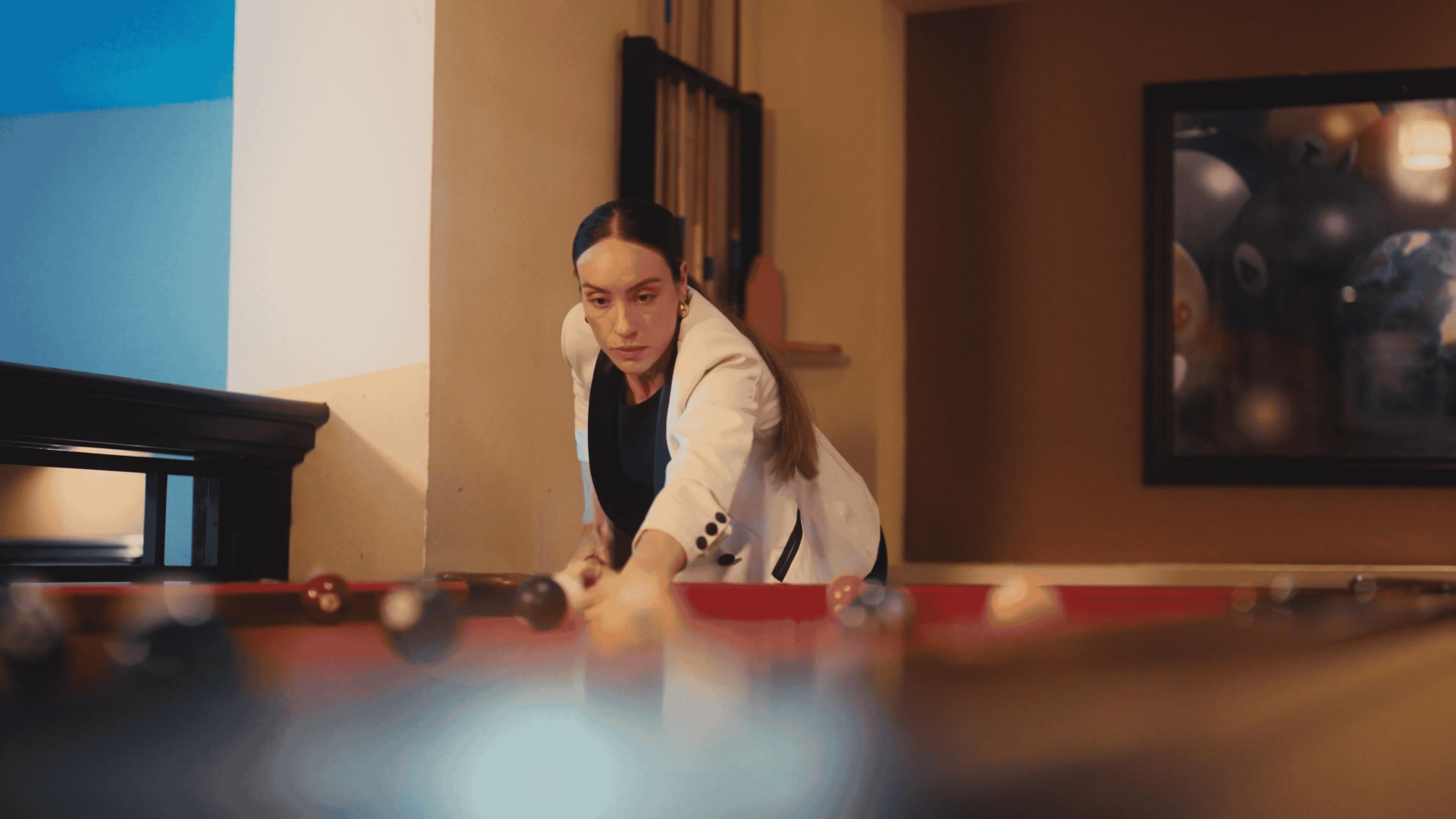 Une personne joue au billard dans une pièce dont un mur est bleu et où est accroché un tableau encadré.