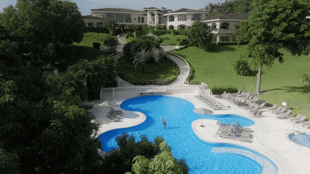 A large, oval-shaped swimming pool with a central island and a surrounding deck. There are lounge chairs and umbrellas around the pool. - Occidental Papagayo - Adults Only - All inclusive (Sardinal)
