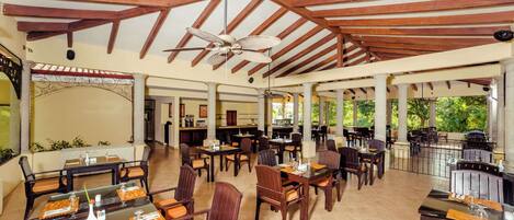 A covered outdoor dining area with wooden beams, tables with chairs, and a ceiling fan.