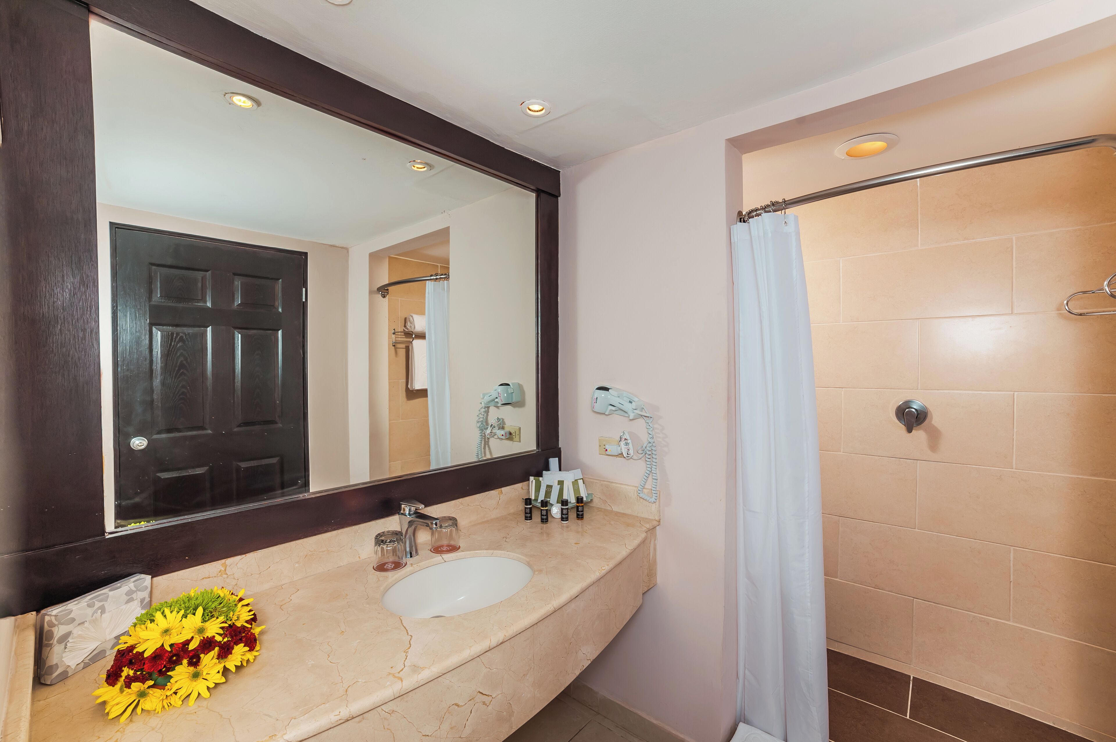 Ein Badezimmer mit großem Spiegel, Waschbecken, Dusche und Handtuchhalter.