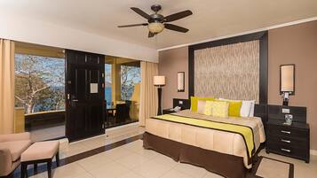 A hotel room with a bed, a desk, a chair, a ceiling fan, and a view of the outdoors.