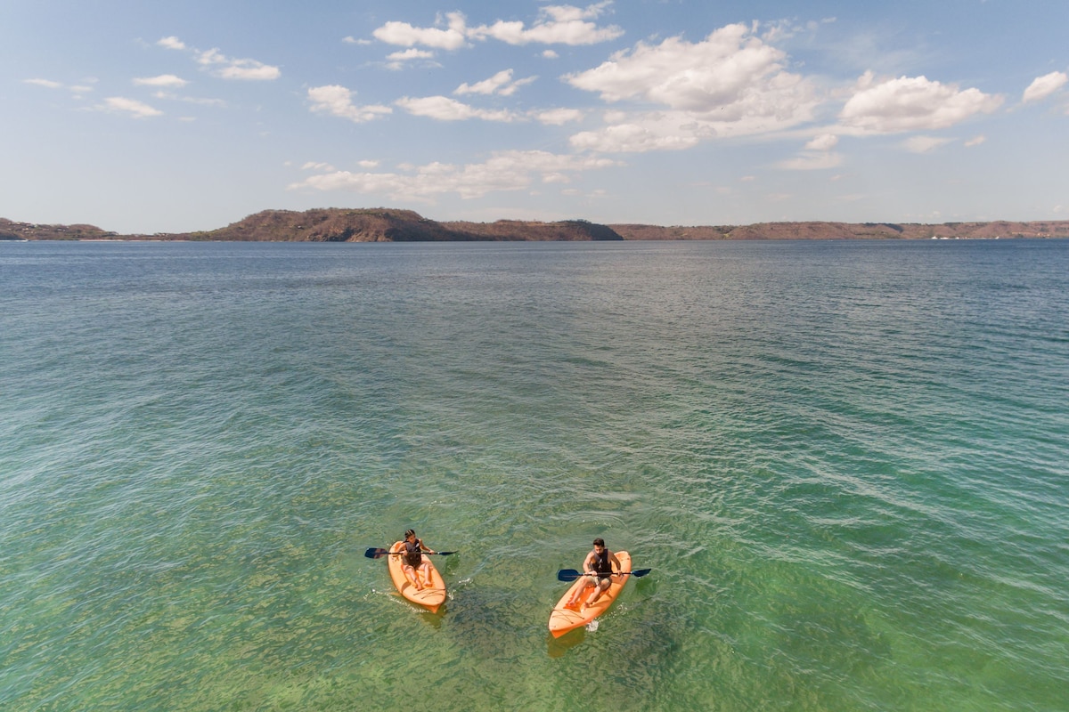 Explore serene waters with kayaks at your doorstep, surrounded by natural hills and a clear view of the sandy bottom.