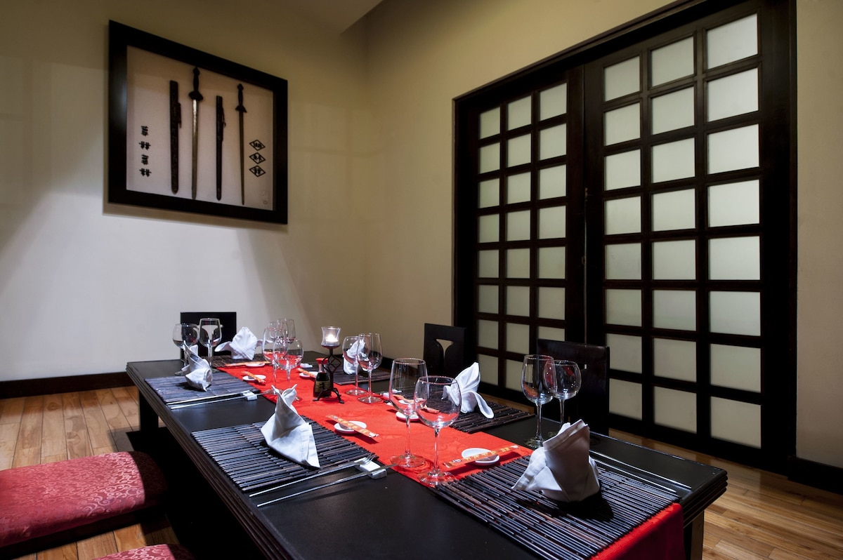 Enjoy a formal dining experience in a traditional Japanese setting with a beautifully set table and elegant artwork.
