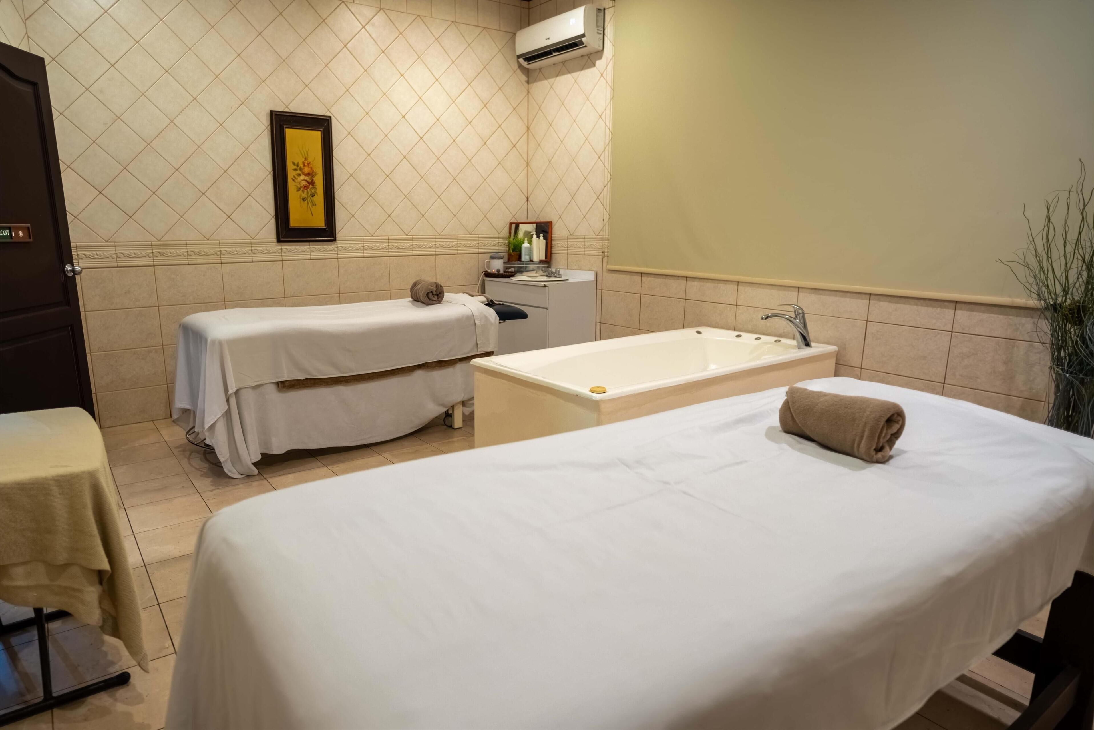 A hotel room with two beds, a bathtub, a small table with toiletries, and a framed picture on the wall.