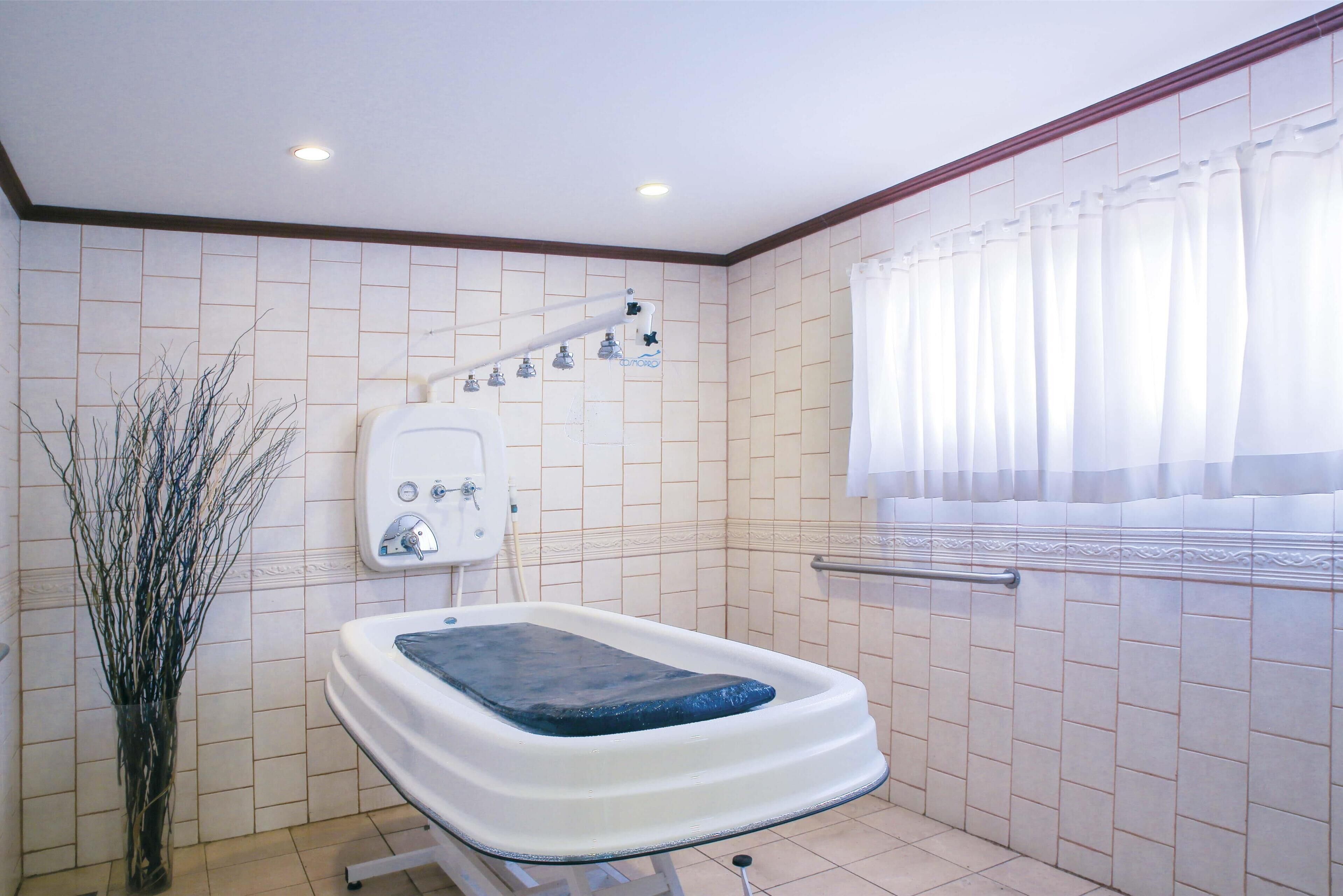 A bathroom with a bathtub, a showerhead, and a window with curtains.