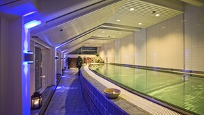 A corridor with a pool, tiled walls, and a ceiling with linear lighting.