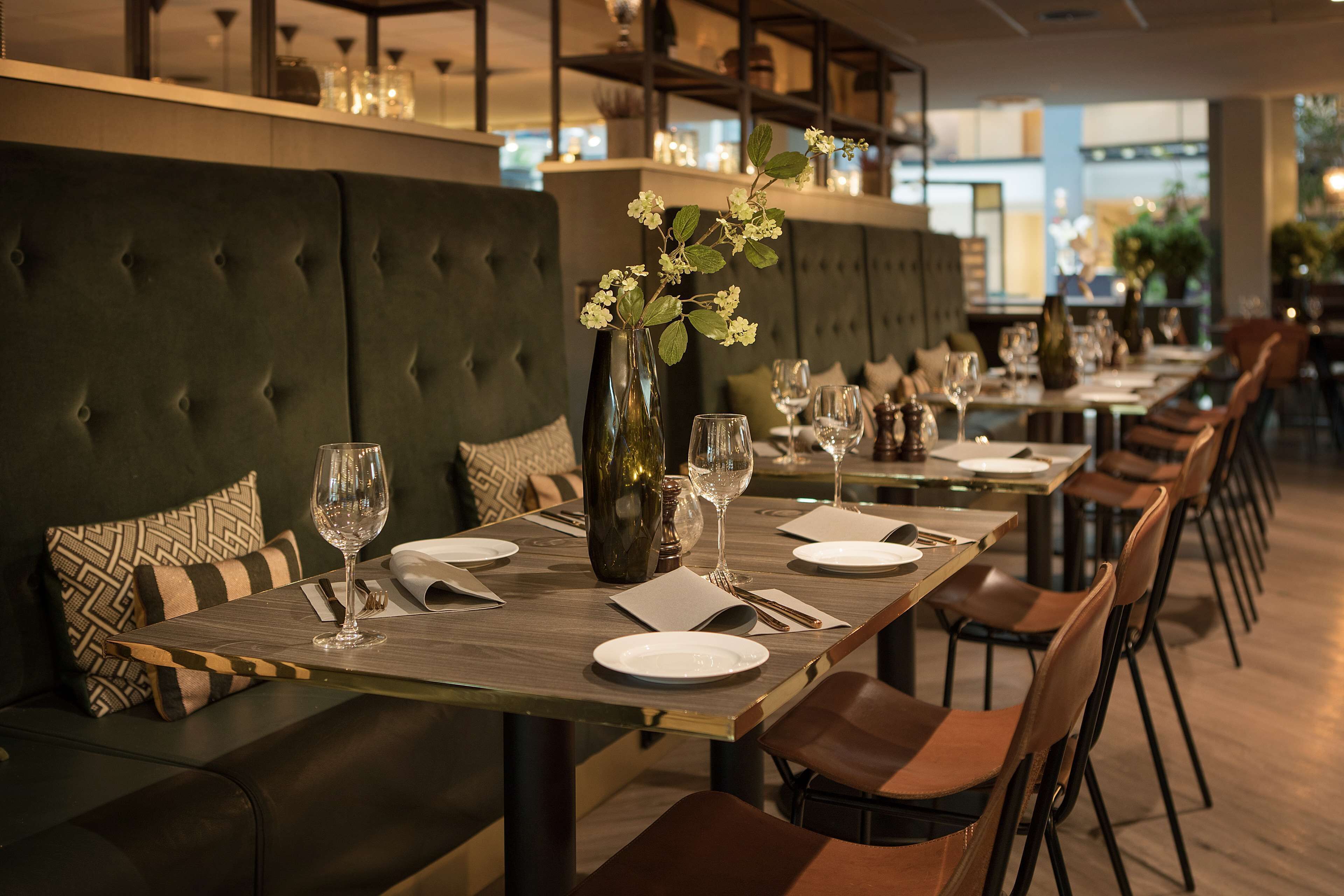 A restaurant with a long dining table set for a meal, cushioned seating, and a vase with flowers.