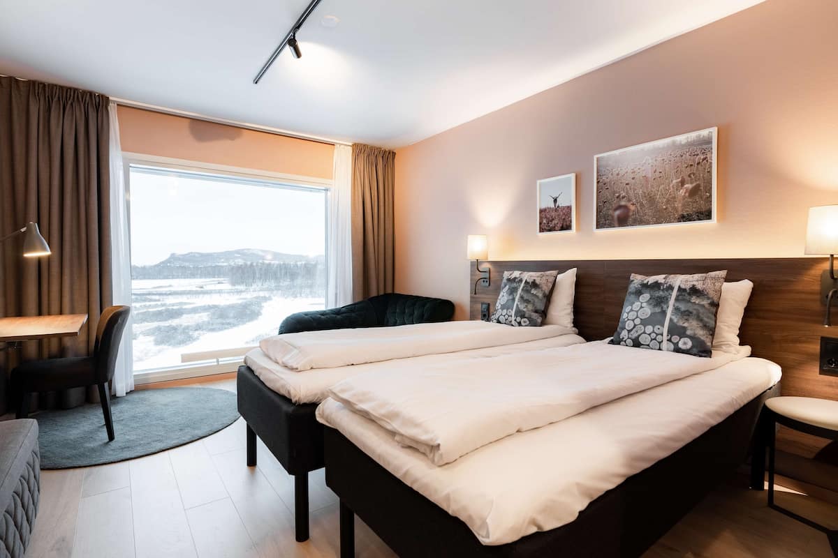 Une chambre d’hôtel avec un grand lit, un bureau et une chaise. Il y a deux lampes fixées au mur et deux tableaux encadrés accrochés au mur.