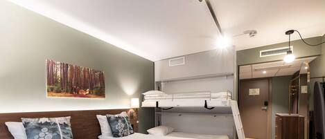 A hotel room with two single beds, a bunk bed, a large mirror, and a painting of a forest.