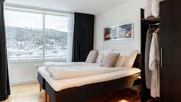 Ein modernes Schlafzimmer mit einem großen Bett, einem Kleiderschrank und einem Fenster mit Blick auf eine verschneite Landschaft.