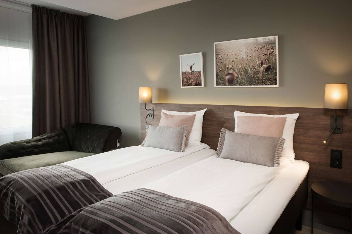 Une chambre d’hôtel avec un grand lit, deux tables de chevet, une tête de lit et deux lampes fixées au mur.