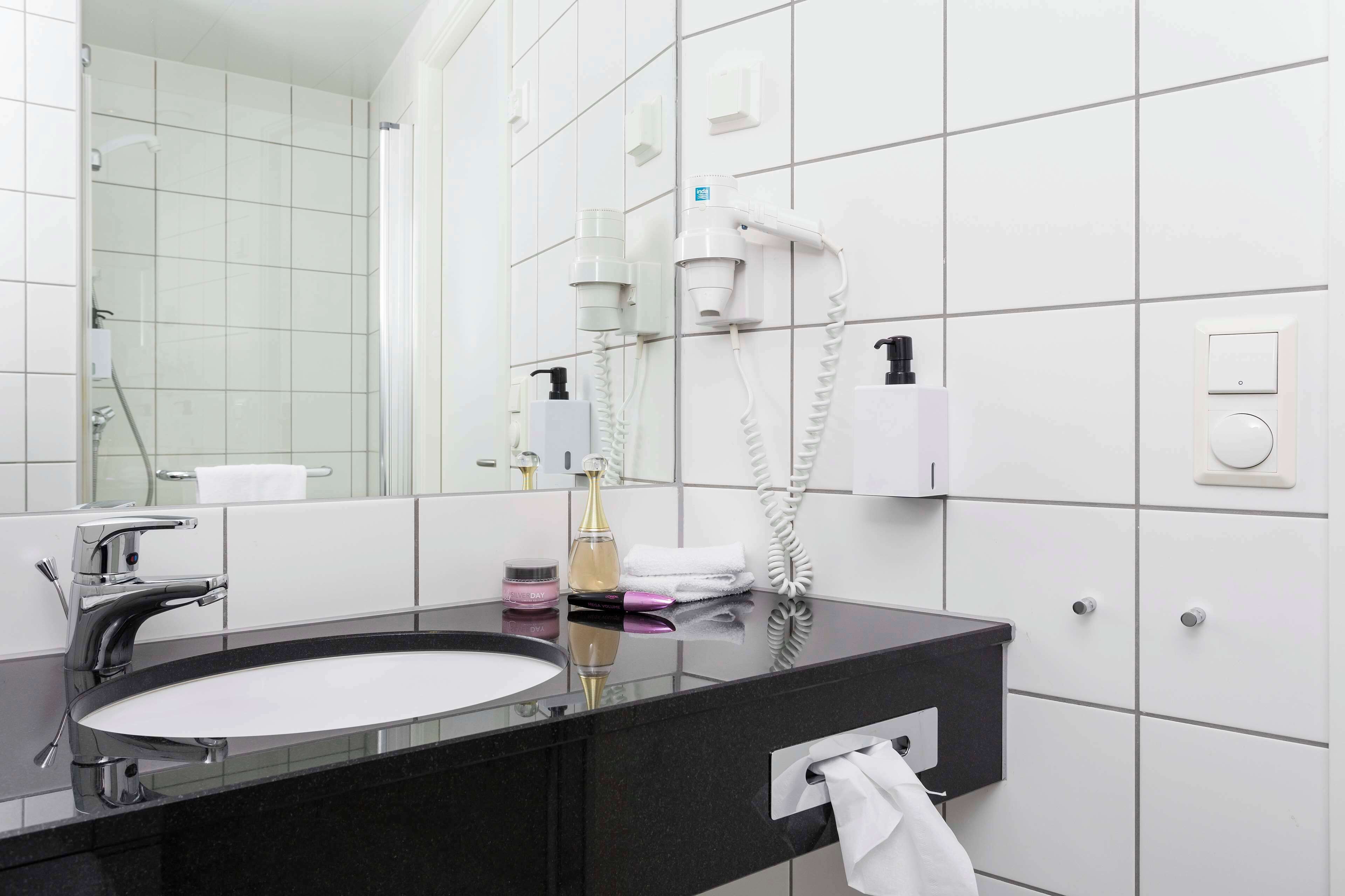 A modern bathroom with a black countertop sink, a large mirror, and a hairdryer mounted on the wall.