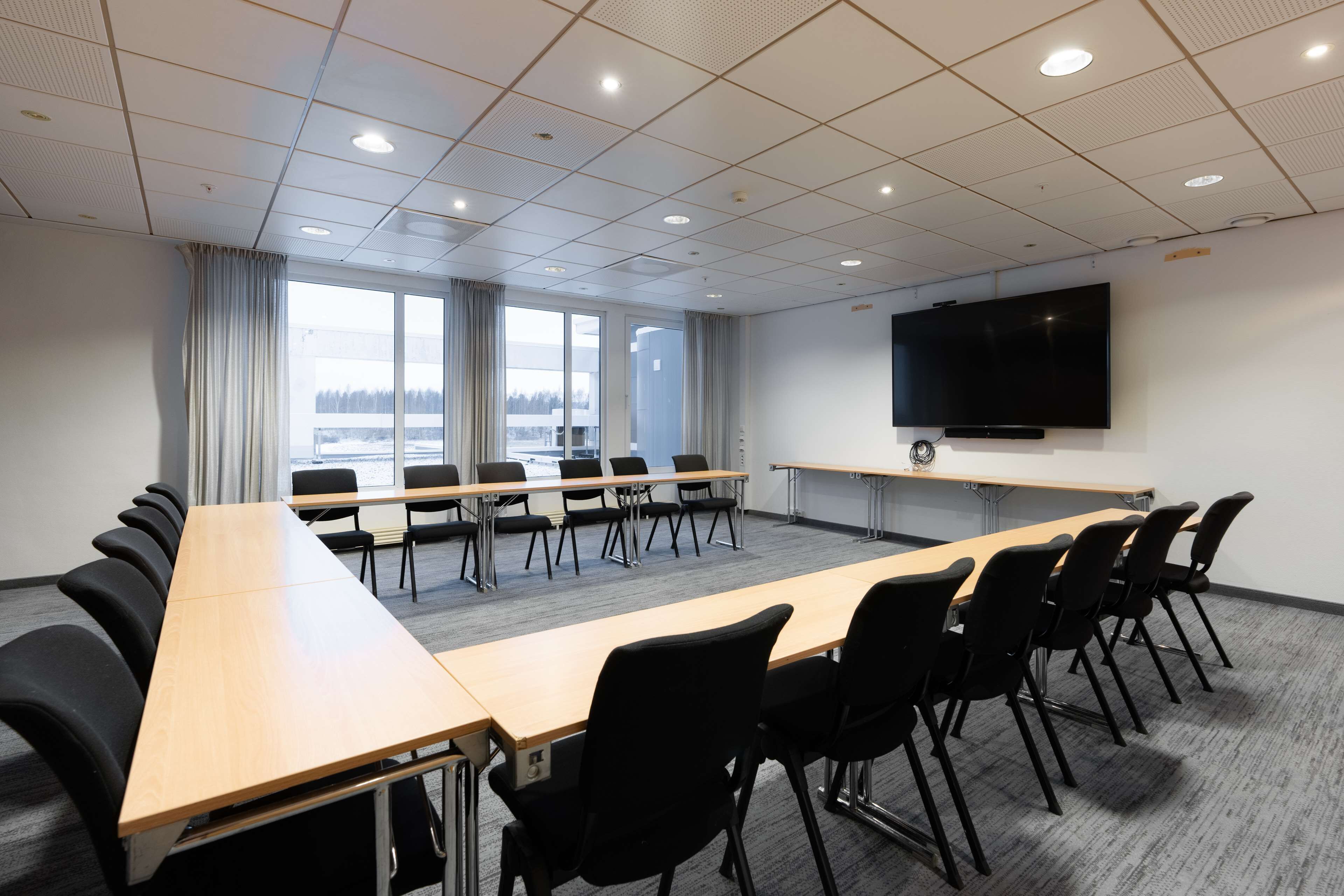 A conference room with a long table, chairs, a large screen, and windows with curtains.