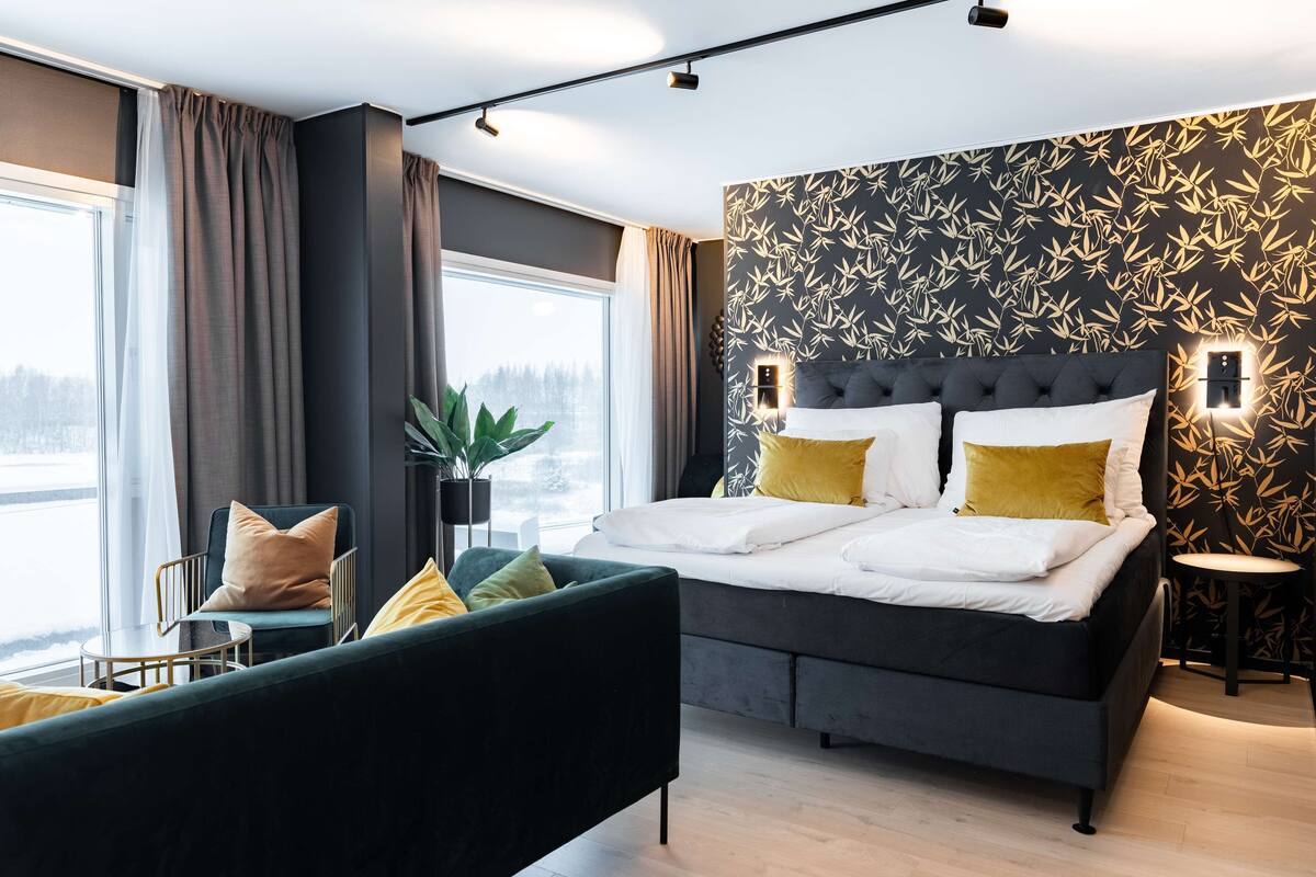Une chambre à coucher moderne avec un grand lit, une tête de lit sombre et une fenêtre avec des rideaux.