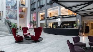 A spacious lobby with a reception desk, red chairs, and a large mural on the wall.