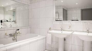 A modern bathroom with a large bathtub, two sinks, and a large mirror.