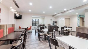 A modern dining area with multiple tables and chairs, a kitchen area, and a seating area with cushioned benches.