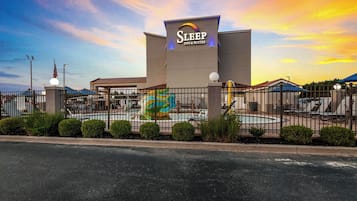 Edificio di Sleep Inn & Suites con insegna, area piscina recintata e cielo al tramonto.