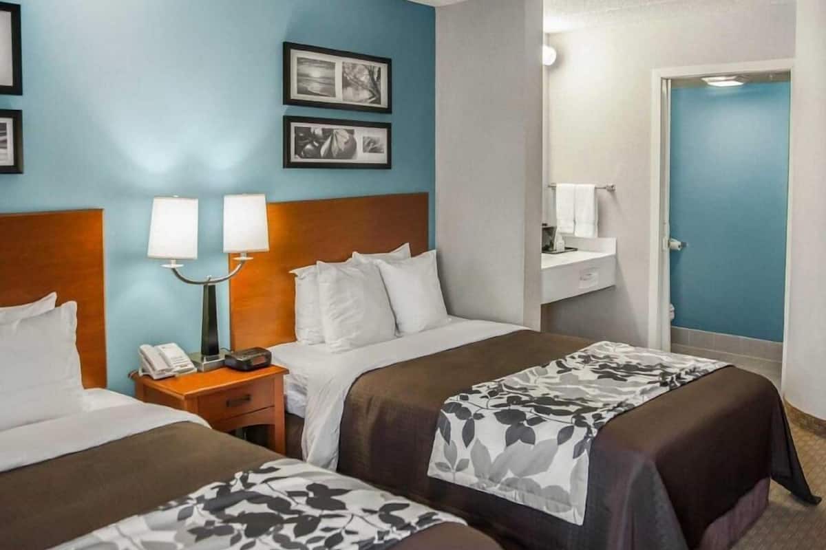 A hotel room with two beds, a nightstand with a phone, a lamp, and a wall-mounted mirror.